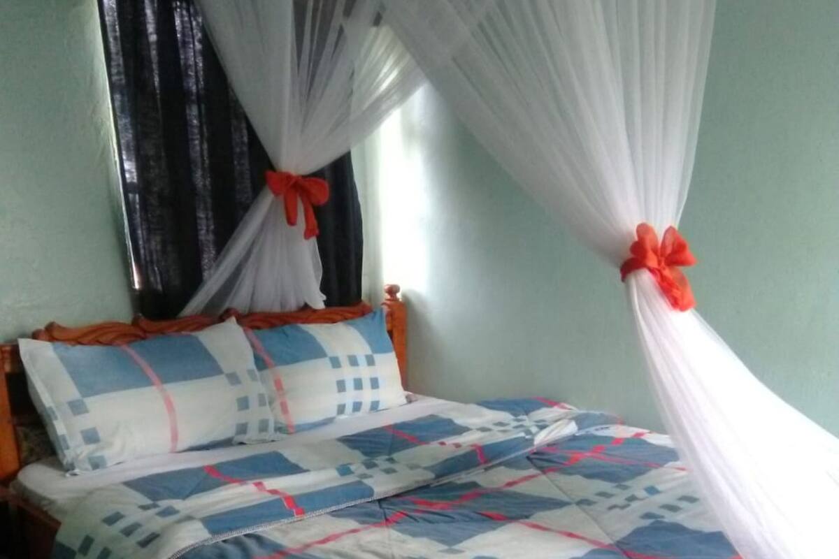 Una cama con colcha azul y blanca, cabecera de madera y dosel blanco con un lazo rojo.