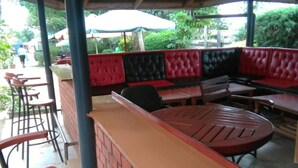 An outdoor seating area with brick walls, red and black cushioned benches, and metal tables. - Usenge Sunset Resort (Usenge)