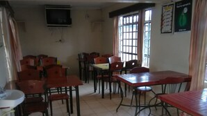 A dining area with multiple tables and chairs, a television mounted on the wall, and a window with curtains. - Usenge Sunset Resort (Usenge)
