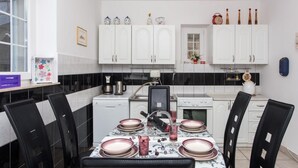 A modern kitchen with white cabinets, a dining table set for four, and various kitchen appliances. - Villa Vista Old Town (Konavle)