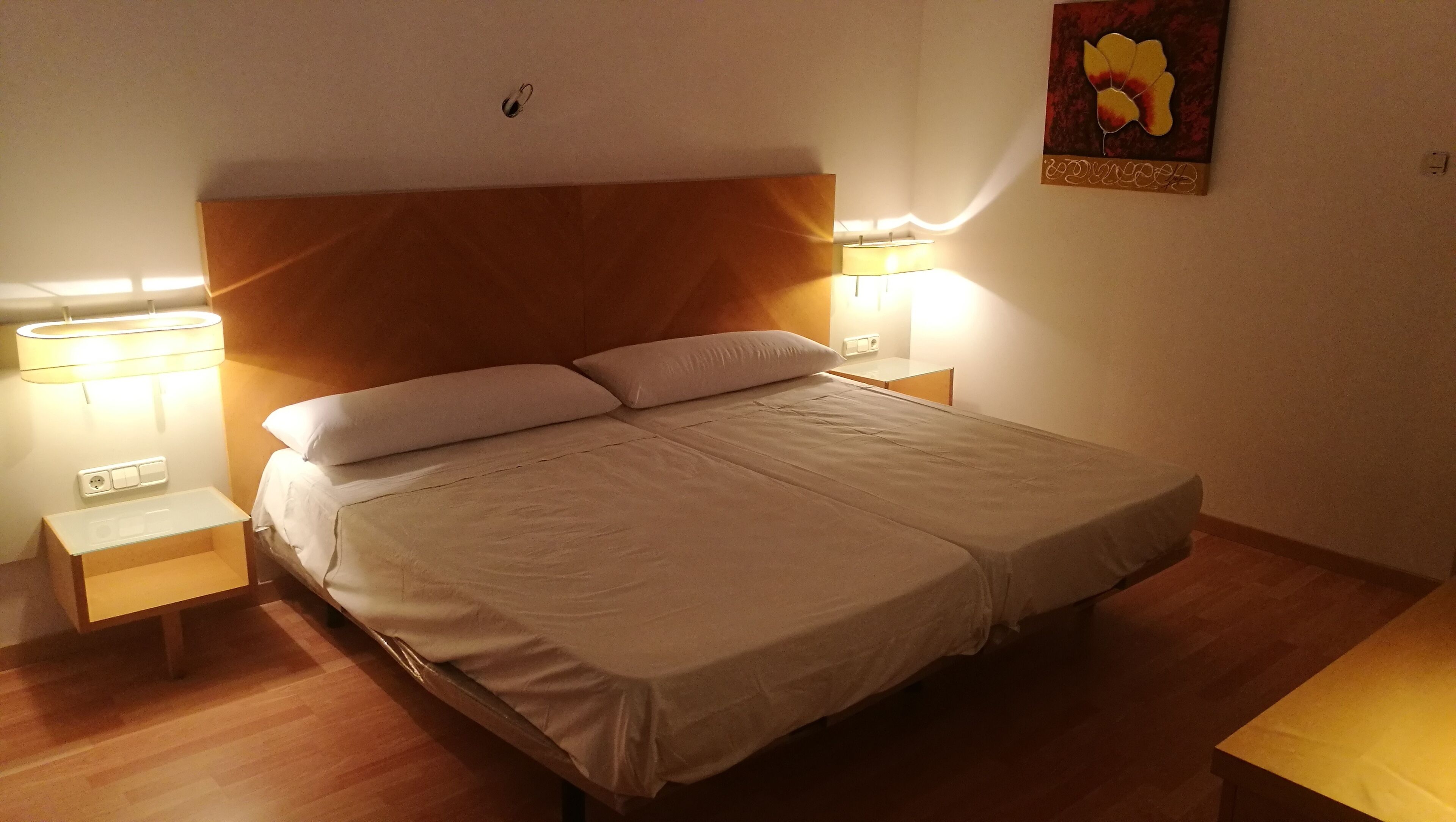 Un lit bien fait, avec deux oreillers, une tête de lit en bois et deux lampes de chevet.