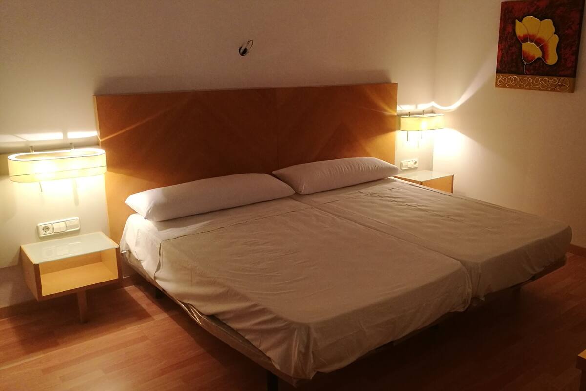 Un lit bien fait, avec du linge de lit blanc, deux lampes de chevet et une œuvre d’art accrochée au mur.