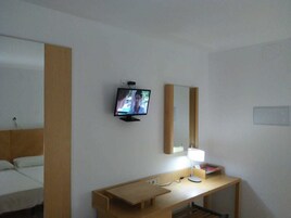 Una habitación de hotel con una cama, un escritorio con lámpara, un televisor y un espejo.