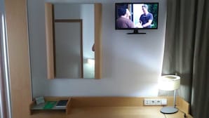 Ein Hotelzimmer mit Holztisch, Wand-Fernseher, Spiegel und Nachttischlampe.