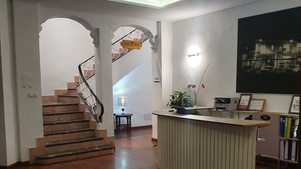 Eine großzügige Lobby mit einer Holztreppe, einem Empfangsbereich und einem großen, gerahmten Bild an der Wand.