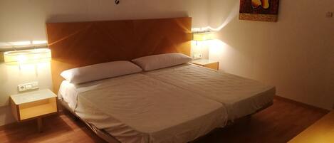 Ein ordentlich bezogenes Bett mit weißen Leinentüchern, zwei Nachttischlampen und einem an der Wand hängenden Kunstwerk.