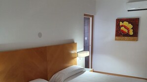 Ein Hotelzimmer mit zwei Einzelbetten, einem Holz-Kopfteil, weißen Bettwäsche, einem Handtuch auf dem Bett, einer Wand-Klimaanlage und einem Gemälde.