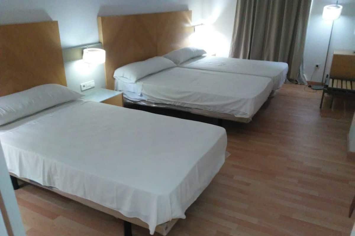 Une chambre d’hôtel avec deux lits simples, des têtes de lit en bois, une table de chevet avec une lampe et une chaise.