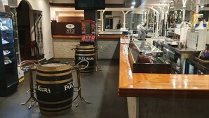 Eine Barbereich mit einer Holztheke, Hockstühlen und einem großen Fass mit dem Aufdruck 'PATA NECRA'.