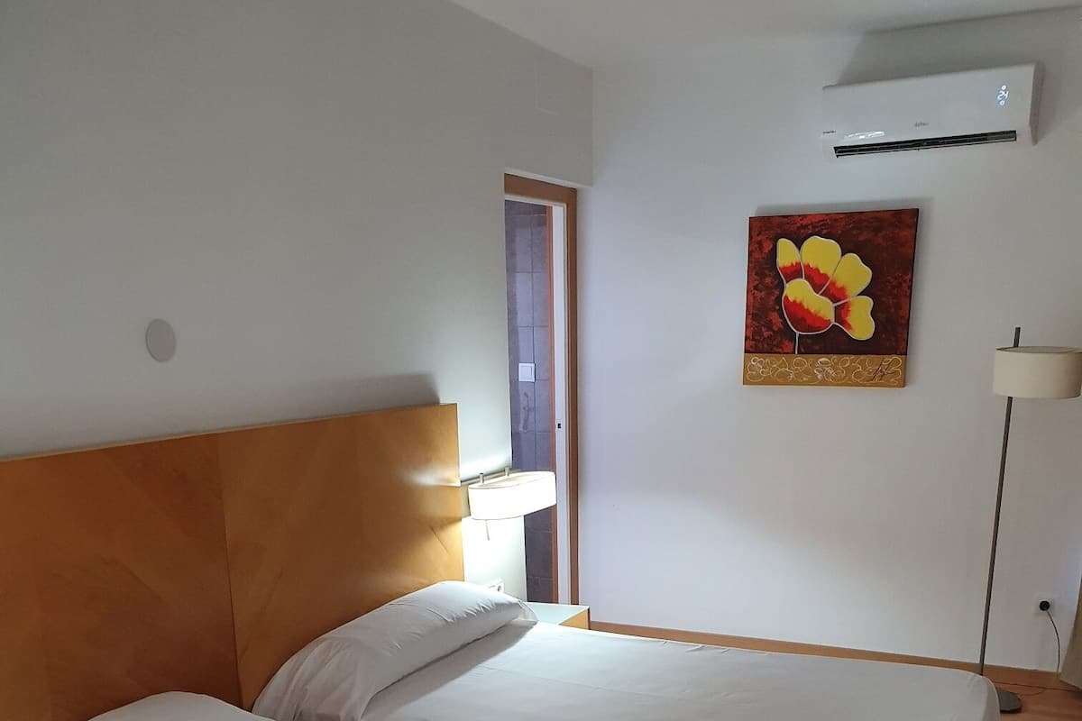 Une chambre d’hôtel avec deux lits, une tête de lit en bois, une serviette blanche sur le sol, un tableau au mur et un appareil de climatisation.