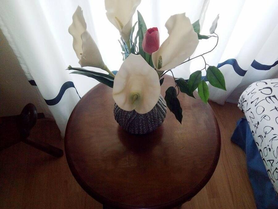 Une table en bois sur laquelle est posé un vase contenant des fleurs blanches et une seule tulipe rose.