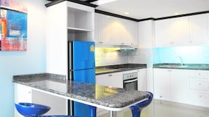 A modern kitchen with white cabinets, a blue refrigerator, and a granite countertop. - Sea View 1-bed at Jomtien Beach - Sleeps 2 (Pattaya)