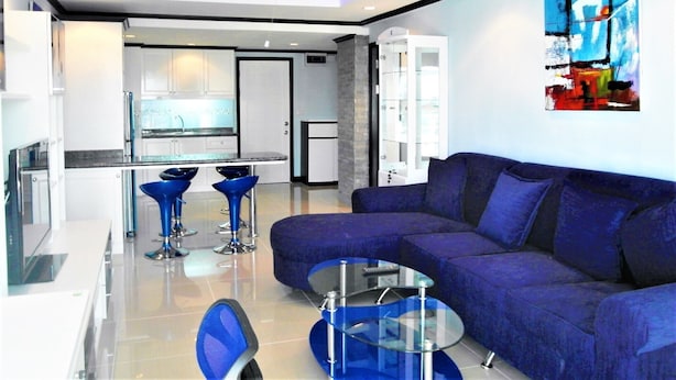 A modern living room with a blue sofa, a glass coffee table, and two blue bar stools. - Sea View 1-bed at Jomtien Beach - Sleeps 2 (Pattaya)
