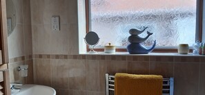 A bathroom with a sink, mirror, and decorative items on the windowsill. - The Hermitage Private Detached Bungalow (Rhyl)