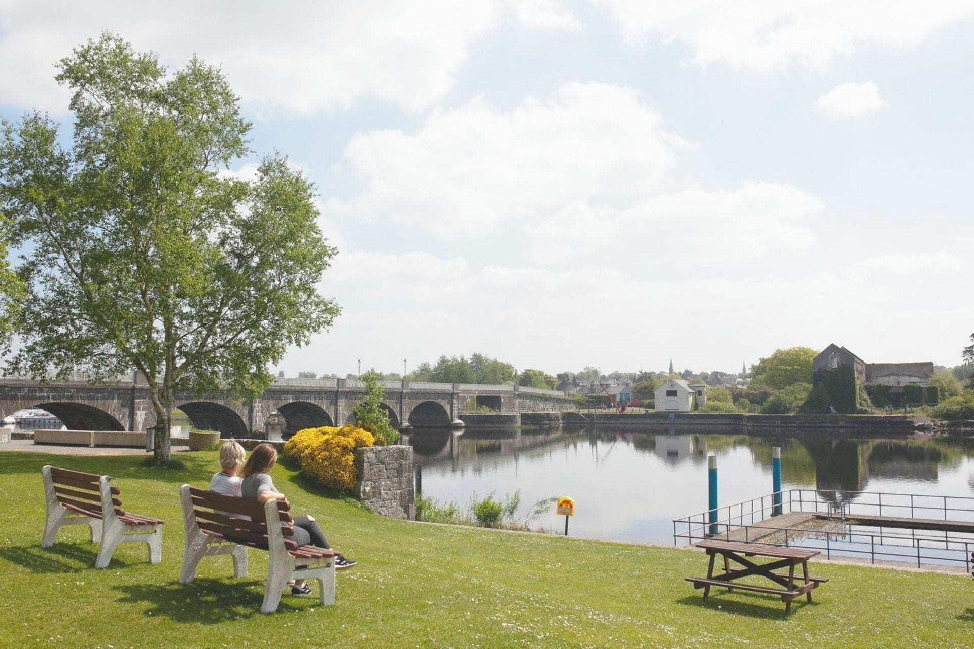 A riverside park with benches, a bridge, and a calm water body.