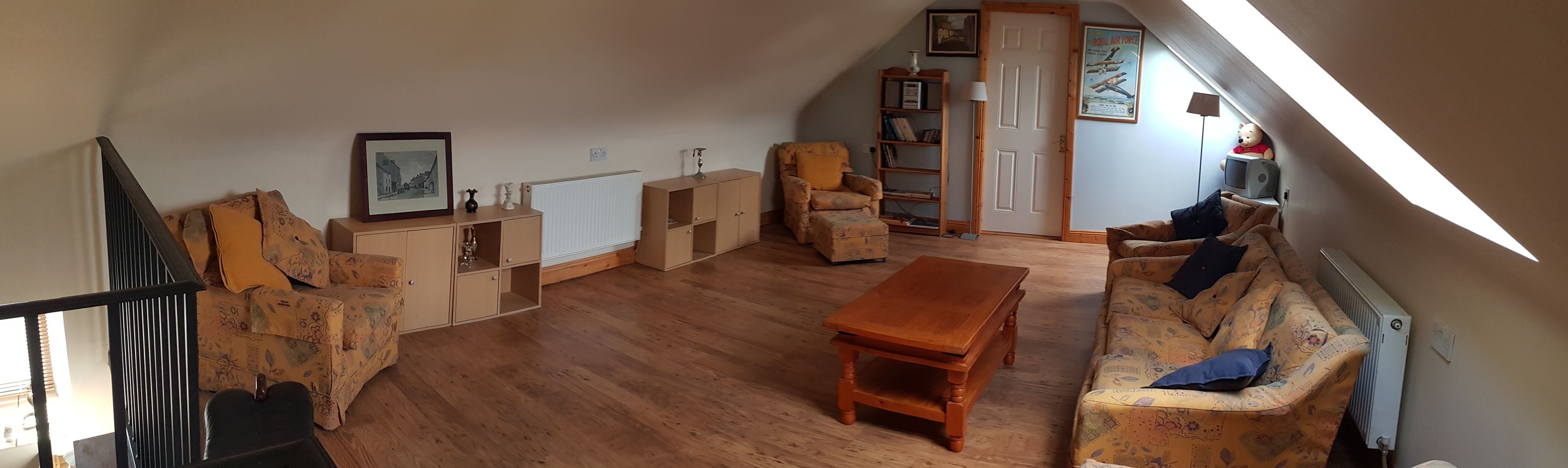 A cozy loft-style living room with a wooden floor, a sofa, a chair, a small table, and a bookshelf.