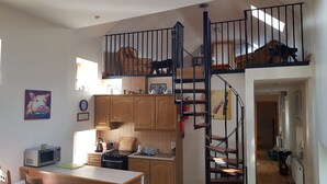 A kitchen with wooden cabinets, a microwave, a kettle, and a sink. There is a staircase leading to a loft area with a bed. - Apartment Sleeps 7 With Mezzanine (Birr)