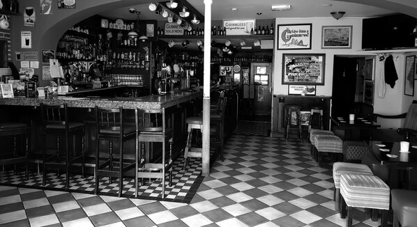 A bar area with a checkered floor, bar stools, and shelves stocked with bottles. - Apartment Sleeps 7 With Mezzanine (Birr)
