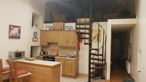 A compact kitchen with wooden cabinets, a small dining area, and a staircase leading to an upper level. - Apartment Sleeps 7 With Mezzanine (Birr)