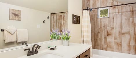 A bathroom with a white sink, dark faucet, wooden wall paneling, a shower curtain, and a mirror with a deer painting.