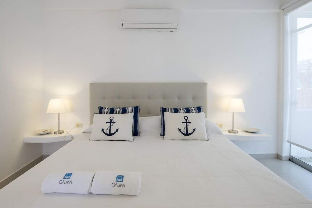 A hotel room with a large bed, two nightstands, two lamps, and a view through a window.