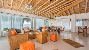 Amplia sala de estar con techo de madera, muebles de mimbre y ventanas grandes que ofrecen vista al mar.