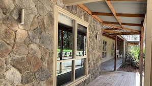 A stone exterior wall with a wooden deck and a covered porch area. - Grand Gippsland Home Sleeps Up To 28 (Trafalgar East)