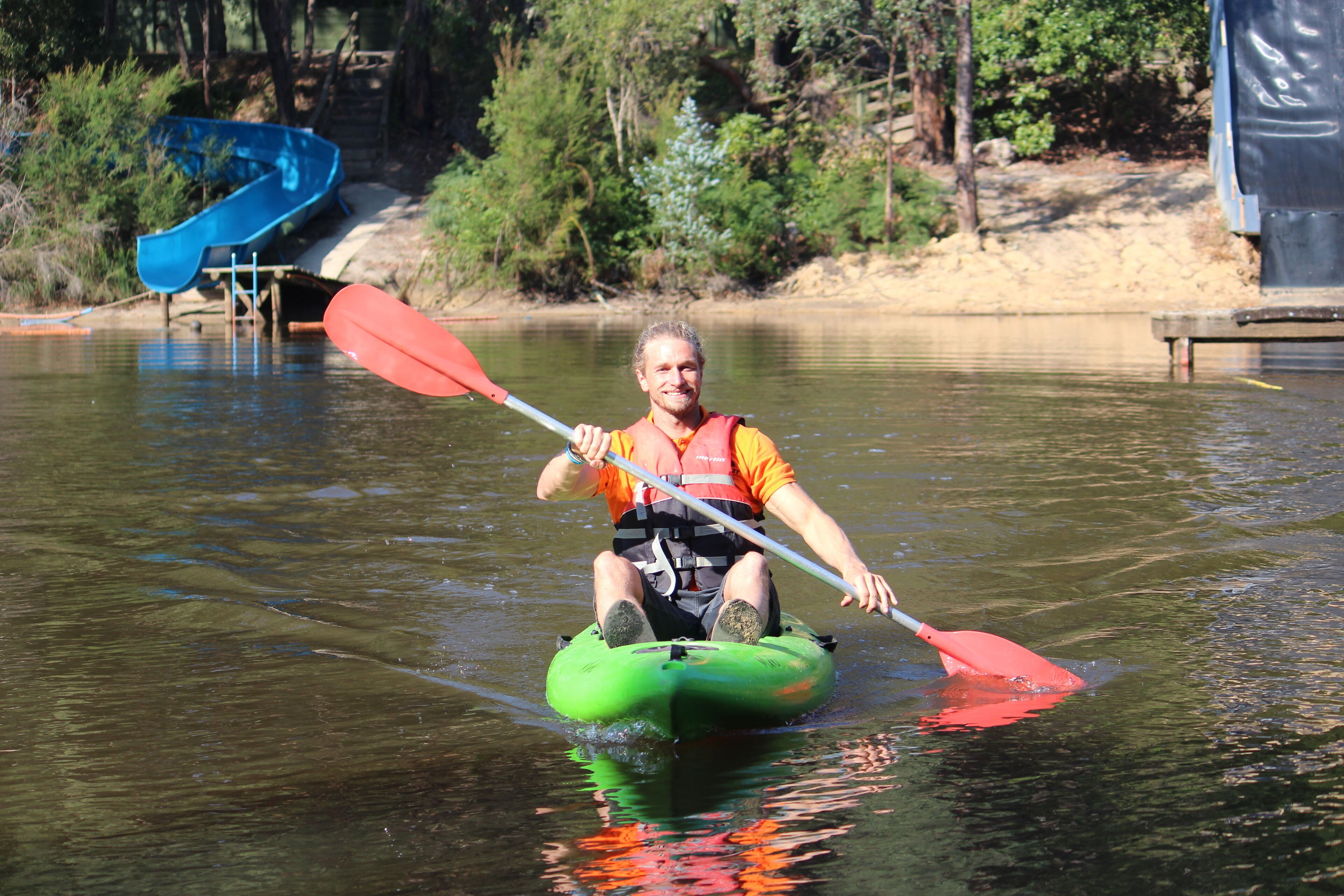 A person on a green inflatable raft in a body of water, holding a red paddle.