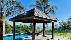 A wooden gazebo with a pool, surrounded by palm trees and a view of the countryside. - Grand Gippsland Home Sleeps Up To 28 (Trafalgar East)