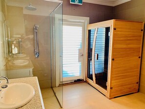 A bathroom with a glass shower enclosure, a sink, and a wooden cabinet. - Grand Gippsland Home Sleeps Up To 28 (Trafalgar East)