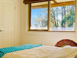 A bedroom with a bed, a window with a view of trees, and a white door. - Grand Gippsland Home Sleeps Up To 28 (Trafalgar East)