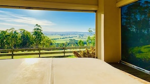 A room with a large window offering a view of a green landscape and a distant horizon. - Grand Gippsland Home Sleeps Up To 28 (Trafalgar East)