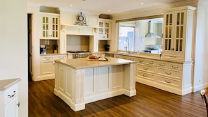 A spacious kitchen with white cabinetry, a large island, and a view to the outside. - Grand Gippsland Home Sleeps Up To 28 (Trafalgar East)