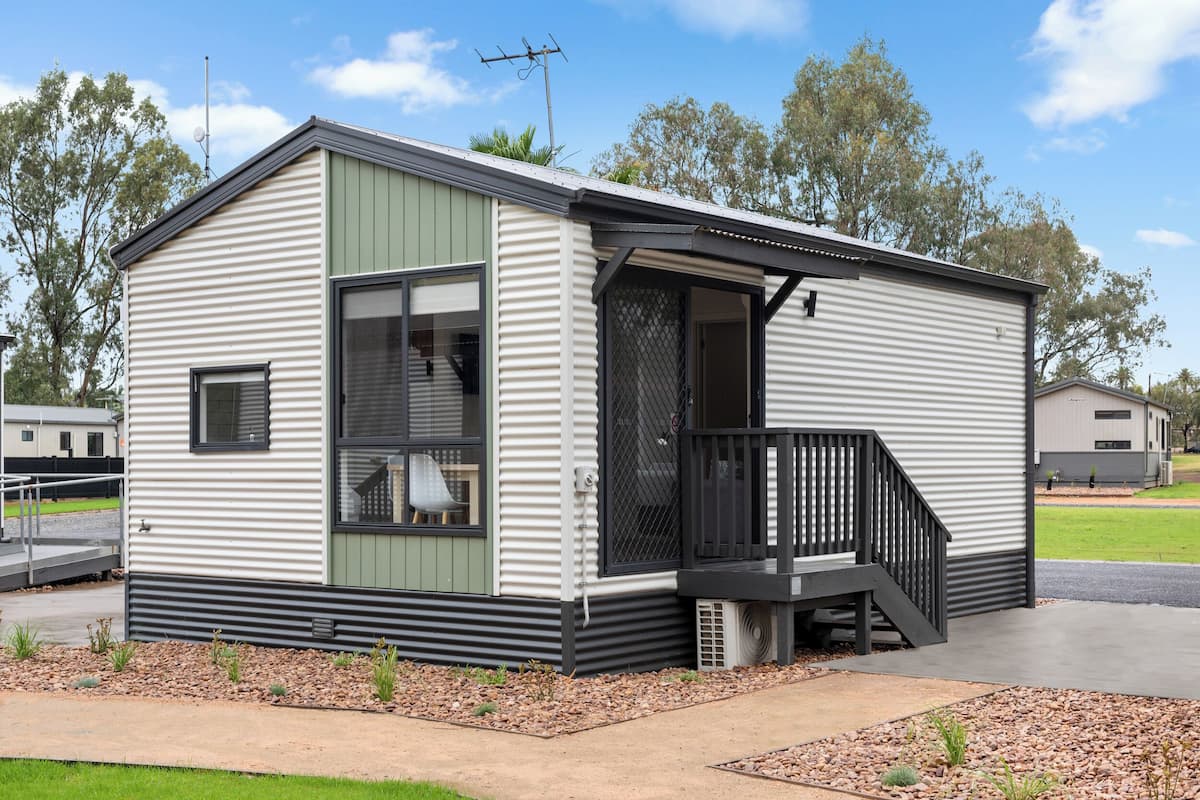 A single-story mobile home with a front porch, large windows, and a small deck.