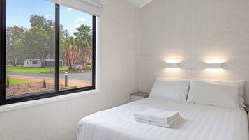 A hotel room with a large window, a neatly made bed, and two wall-mounted lights.