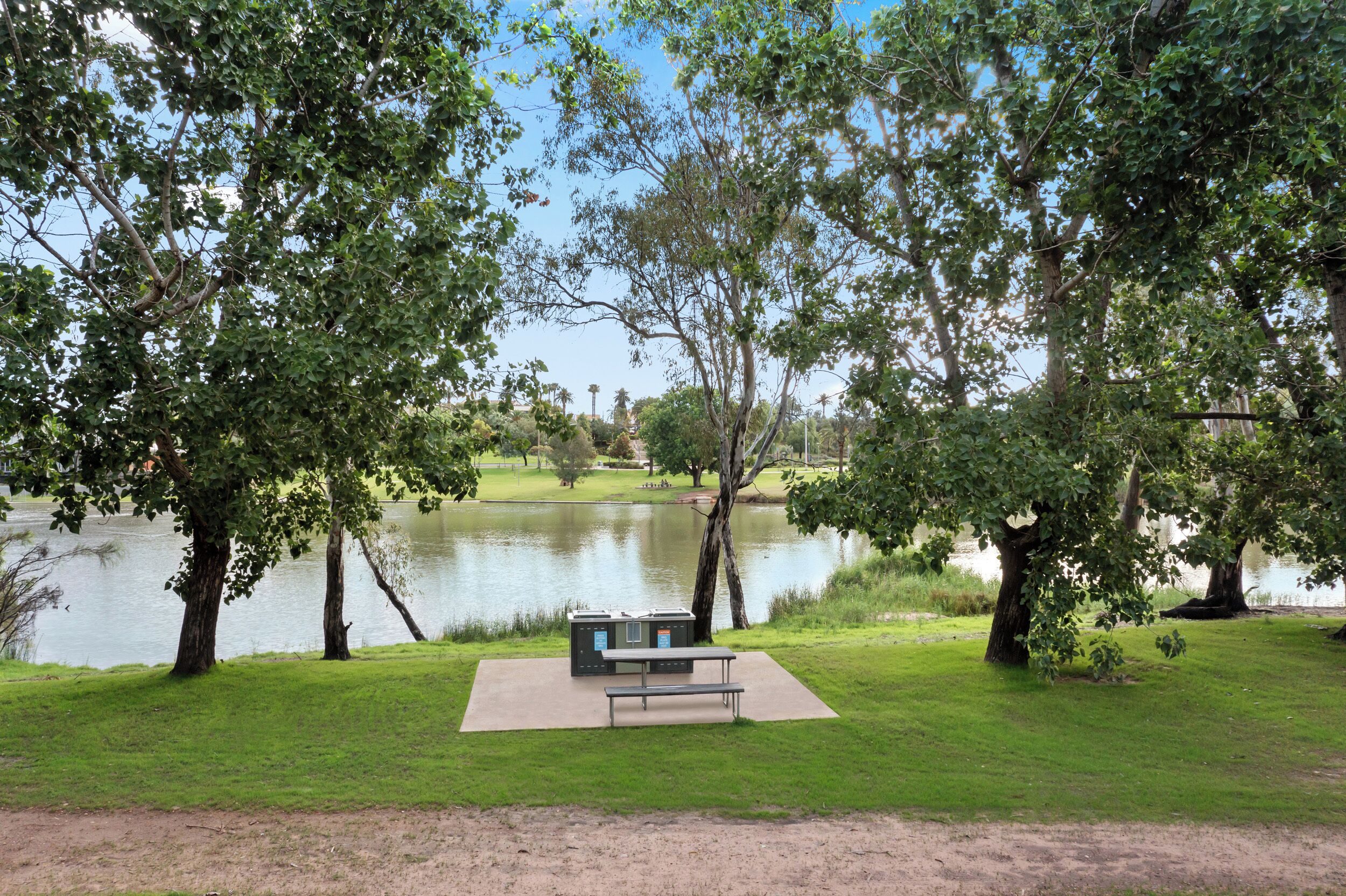 A park with a picnic table and benches, a pond, and trees.