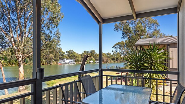 A covered outdoor area with a table and chairs, overlooking a river with a boat. - Discovery Parks - Mildura (Buronga)