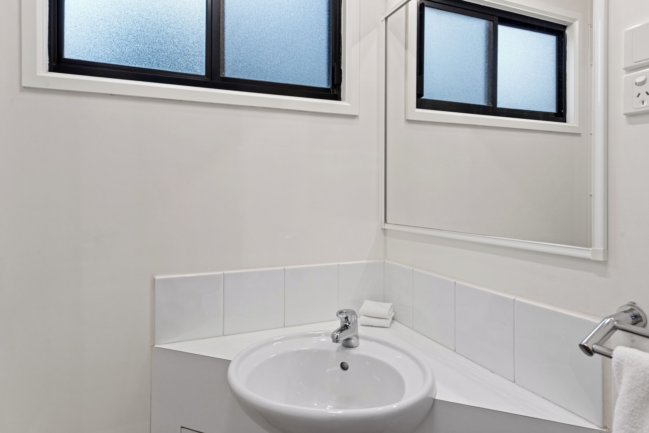 A bathroom with a white sink, a mirror, and a window.