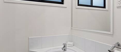 A bathroom with a white sink, a mirror, and a window.