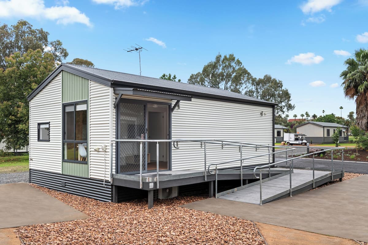 A small, single-story mobile home with a metal exterior, a front porch, and a ramp leading to the entrance.