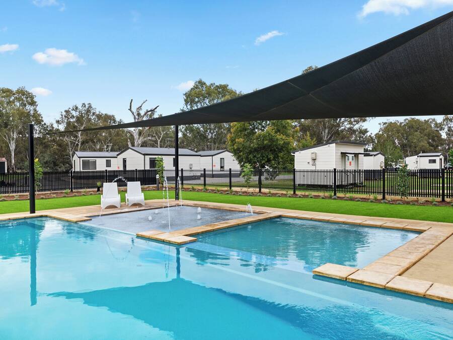 Une piscine avec deux chaises longues, un espace ombragé et une clôture entourant un quartier résidentiel avec des maisons.