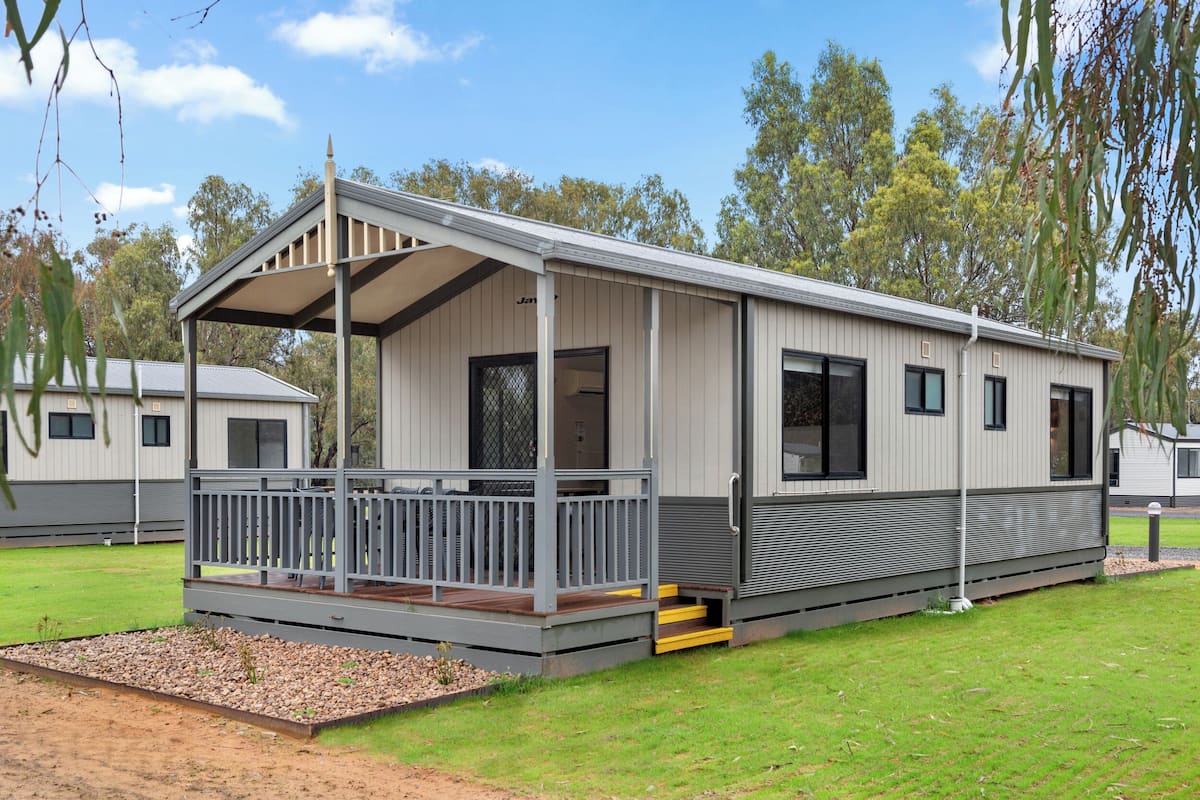 A single-story mobile home with a covered porch, a small deck, and a gravel area in front.