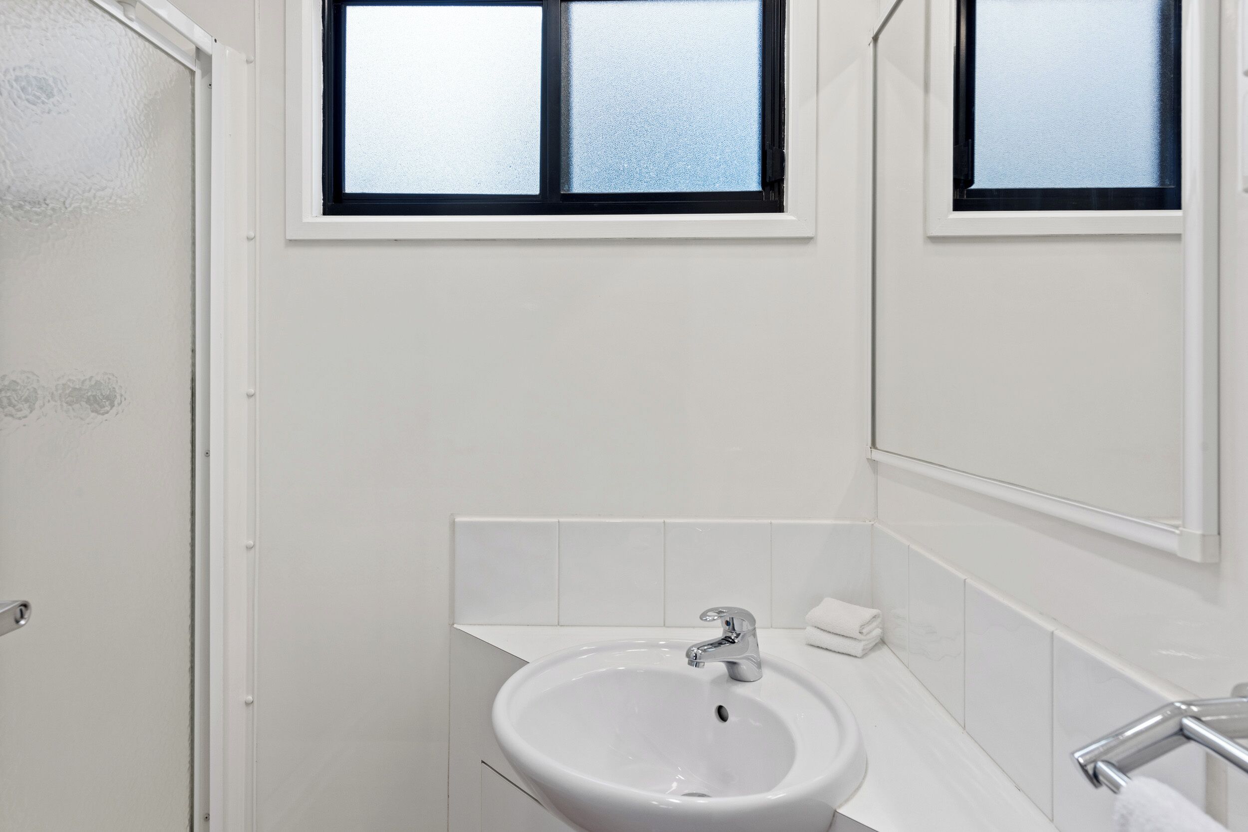 Ein Badezimmer mit einem weißen Waschbecken, einem Spiegel und einem Fenster über dem Waschbecken.