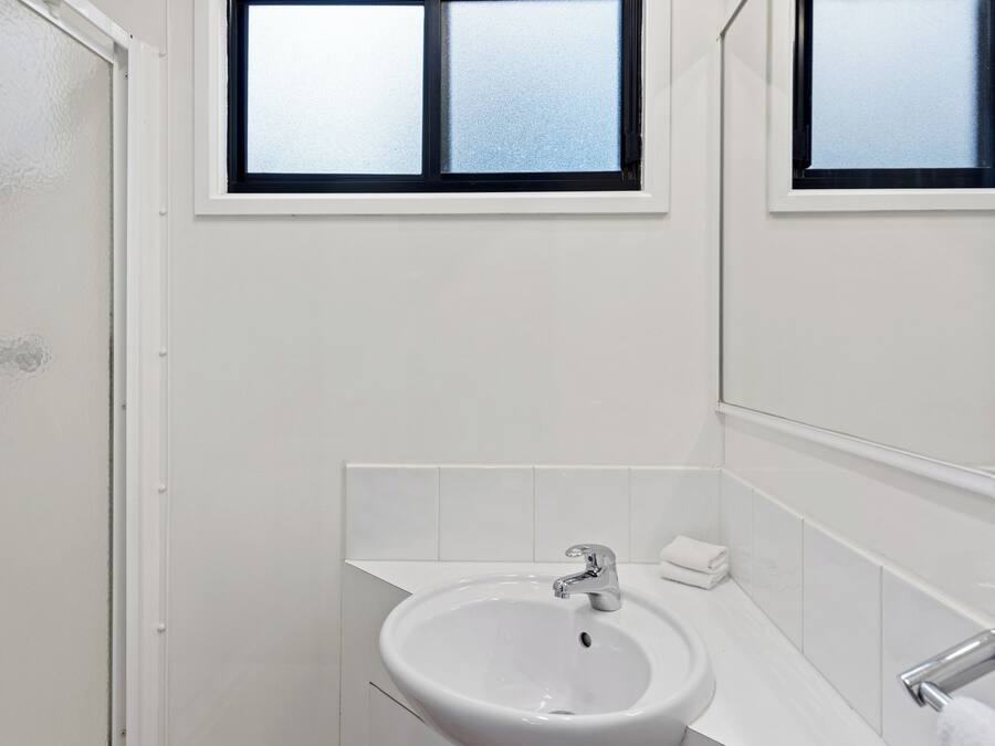 Ein Badezimmer mit einem weißen Waschbecken, einem Spiegel und einem Fenster über dem Waschbecken.