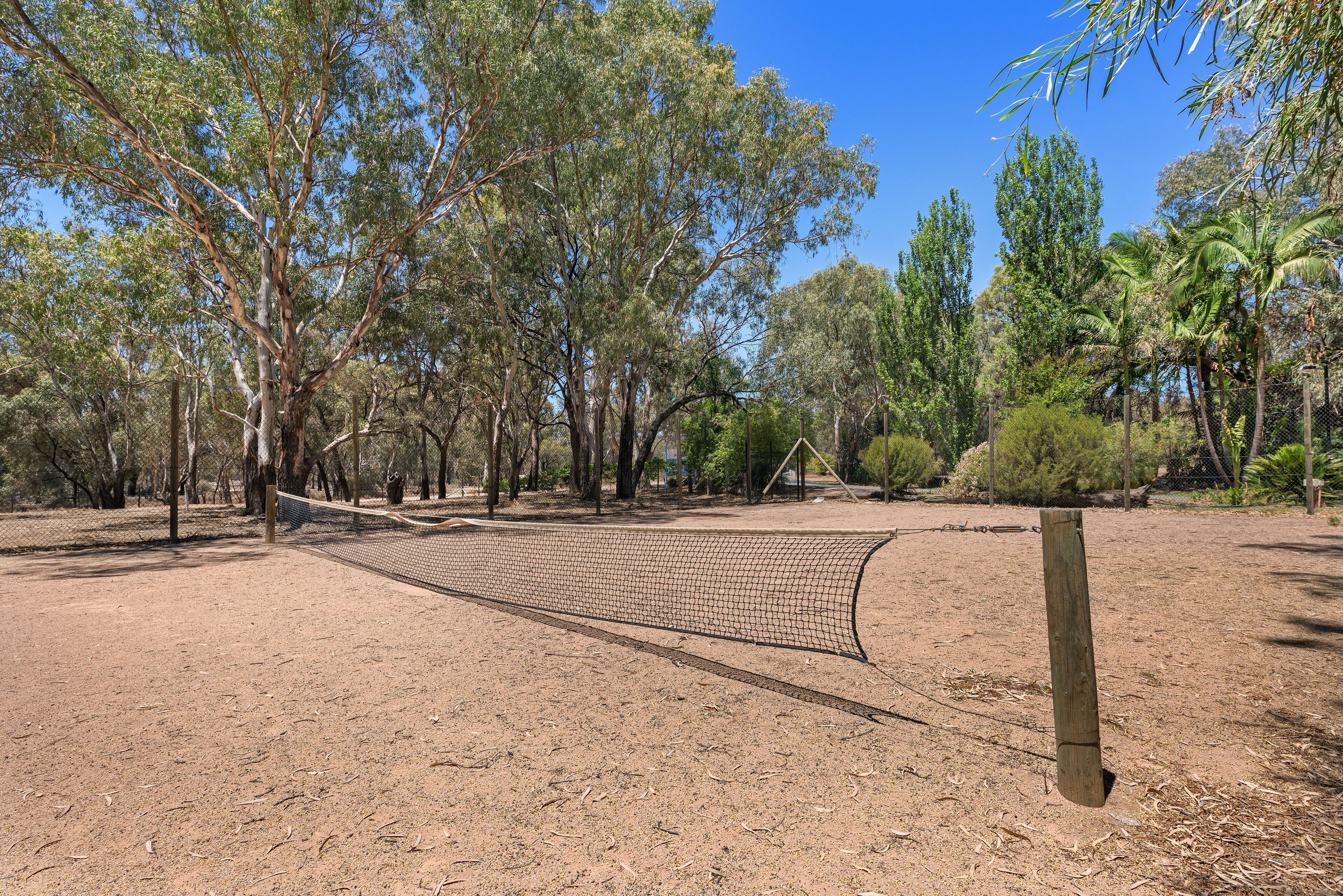 Una cancha de voleibol de tierra rodeada de árboles y una valla de madera.