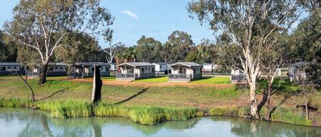 A lakeside view of a campground with several cabins, a grassy area, and trees.