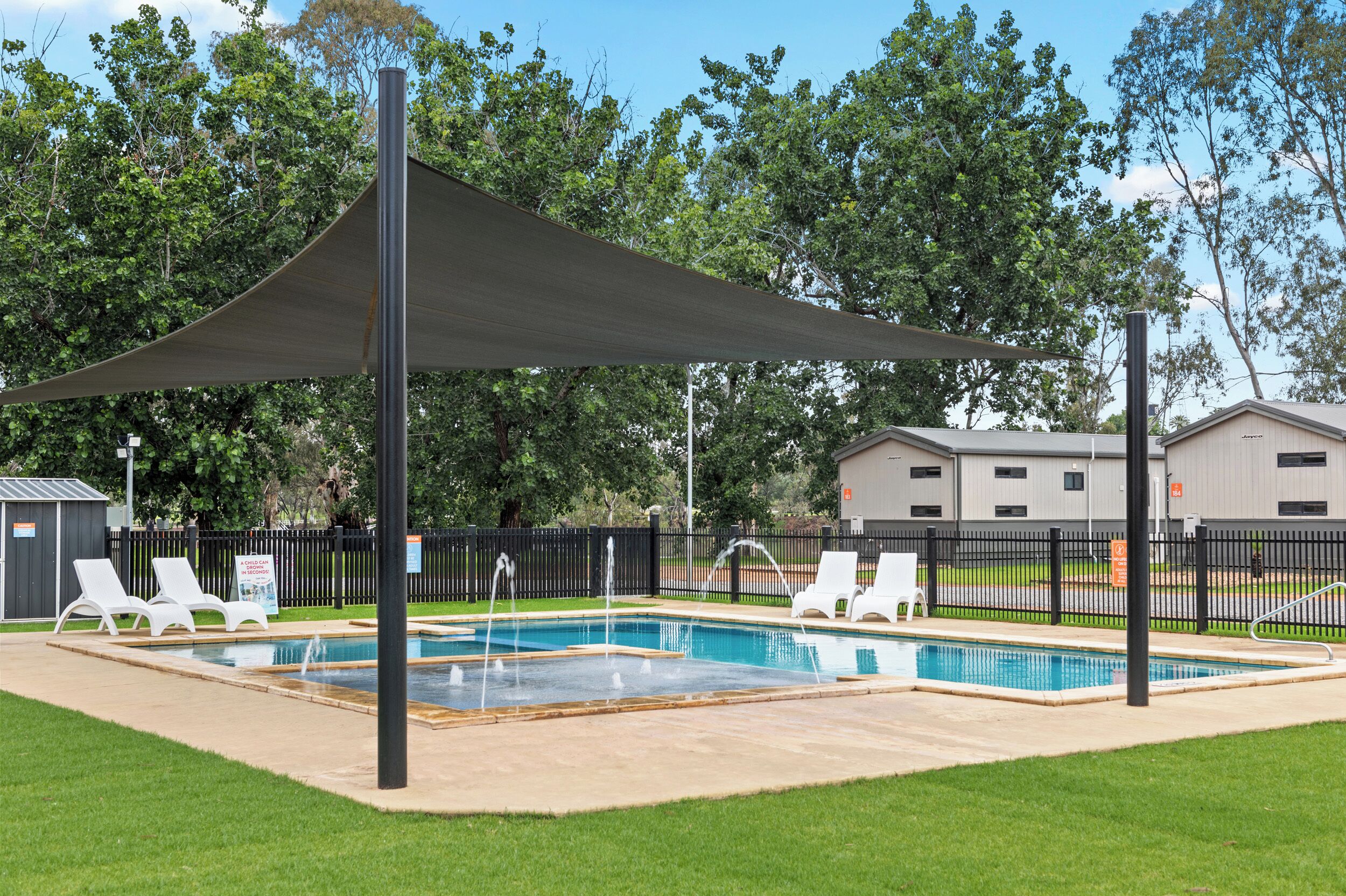 A swimming pool with a canopy, surrounded by white lounge chairs and a fenced area.