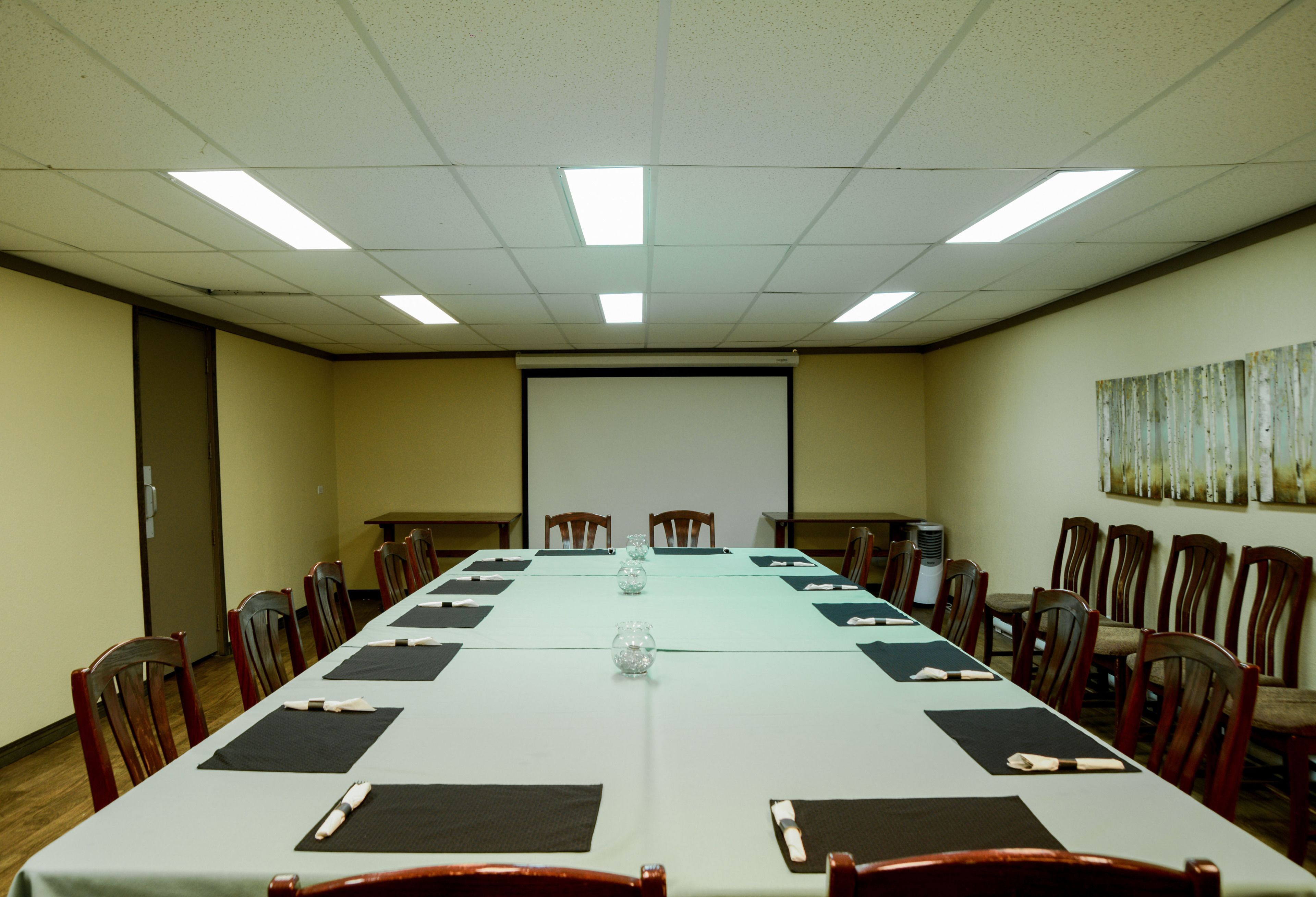 Une salle de conférence avec une longue table, des chaises, un écran de projection et un tableau au mur.