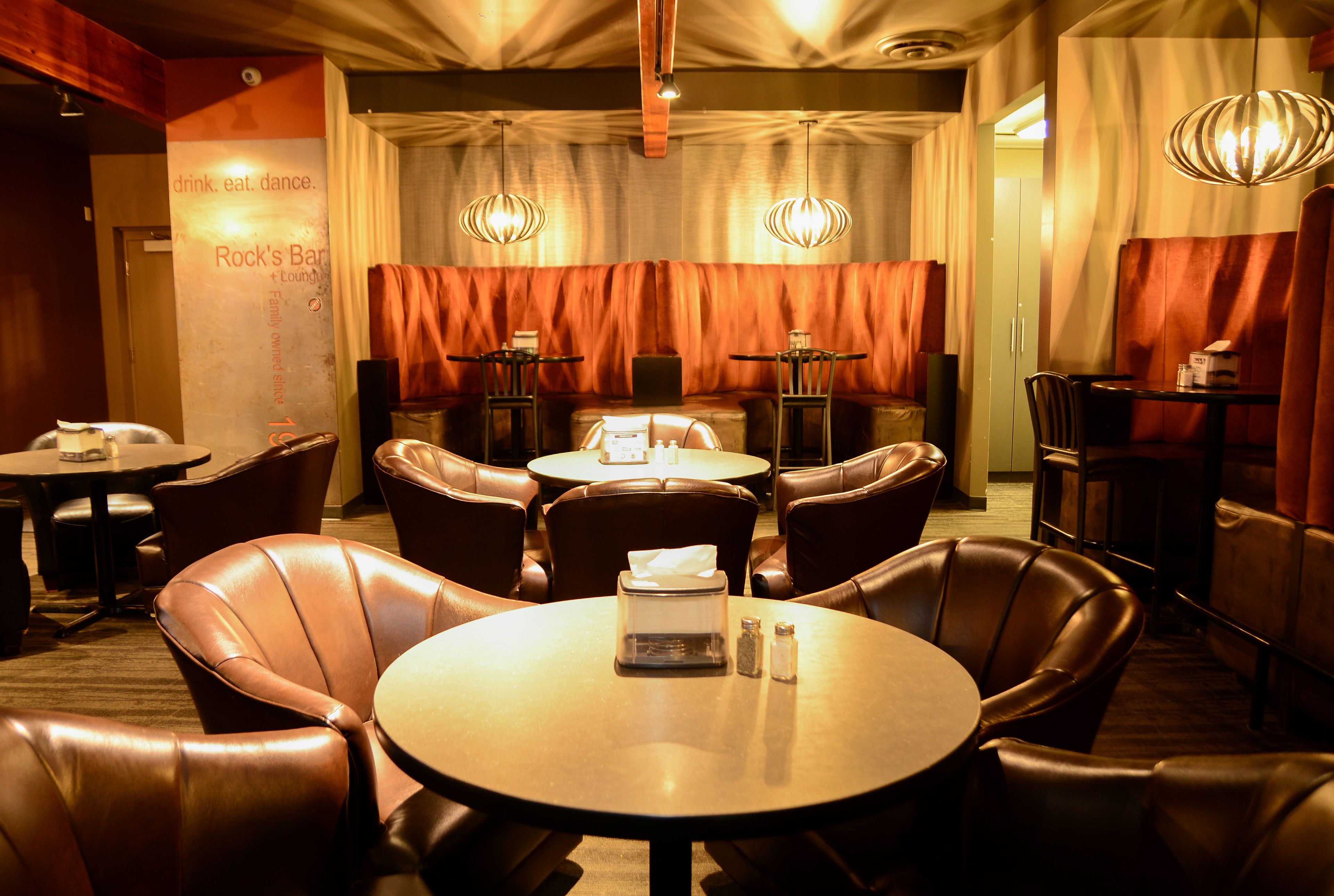 A restaurant with leather booths, round tables, and pendant lighting.