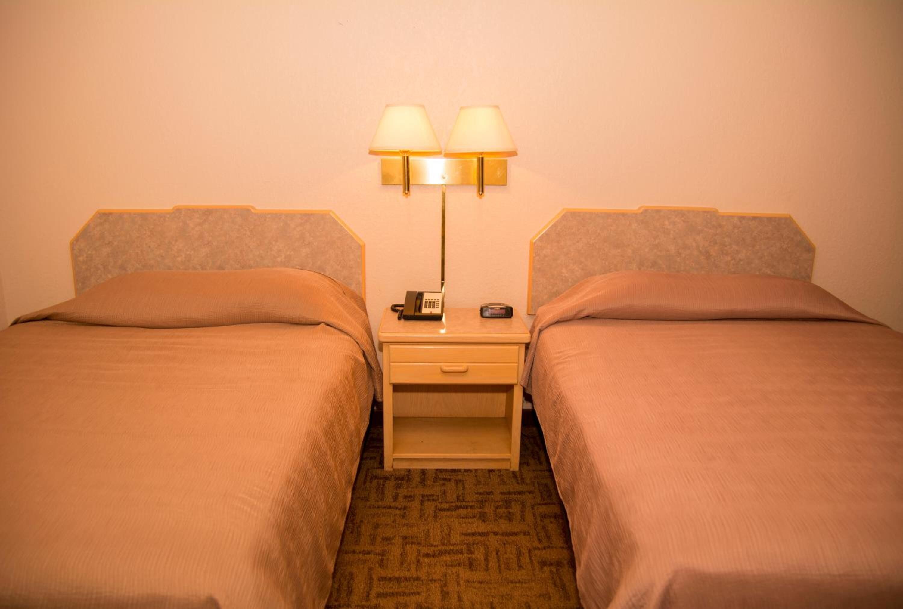 Habitación de hotel con dos camas, cada una con cabecera, mesita de noche con lámpara y teléfono.